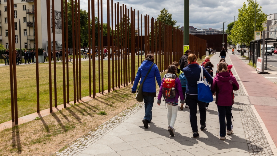 Kinder laufen an der Gedenkstätte an Metallstangen lang, welche die Mauer repräsentieren.