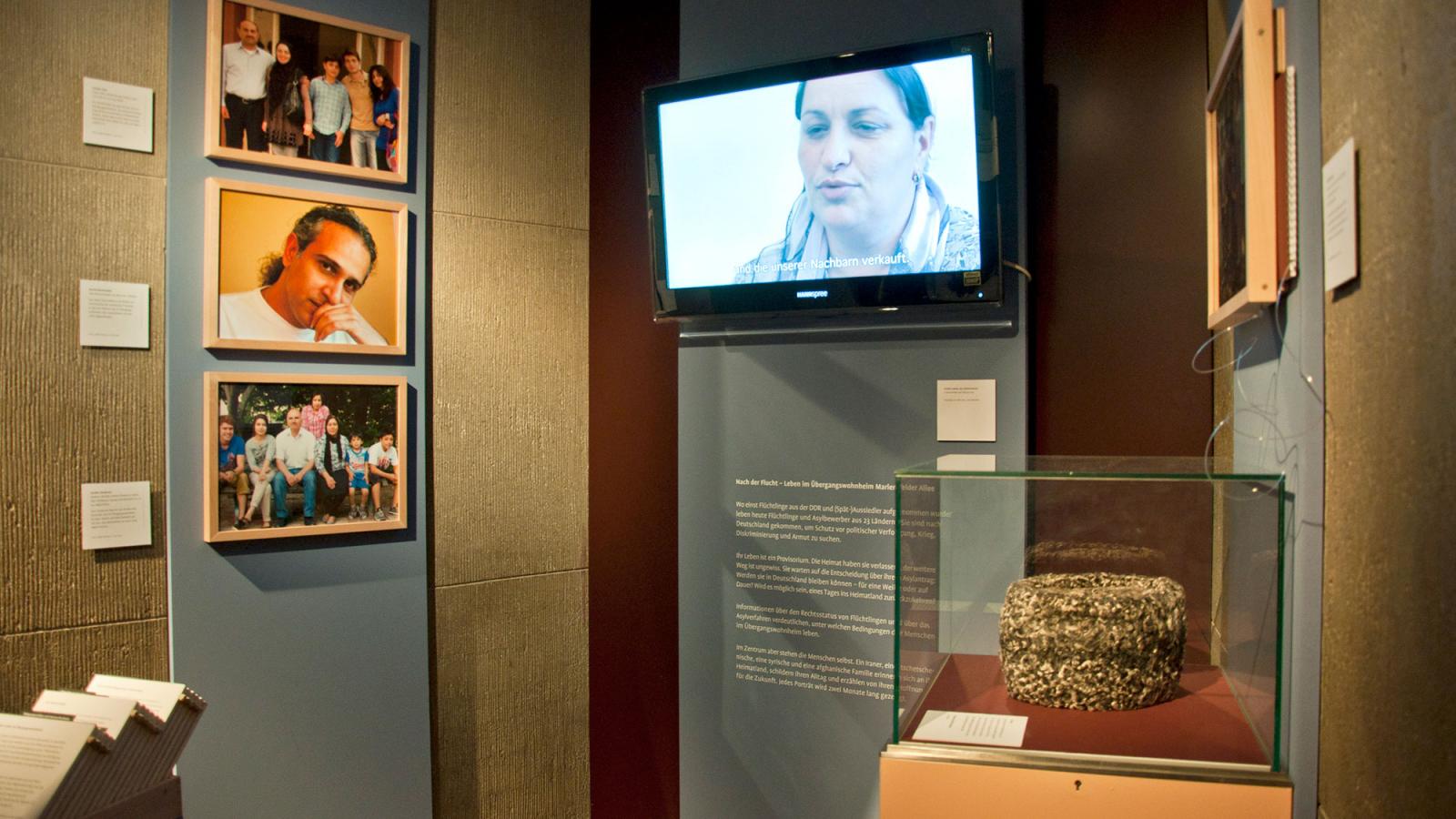 Ausschnitt aus der Austellung mit Fotografien, einem Videoscreen und einer Ausstellungsvitrine.